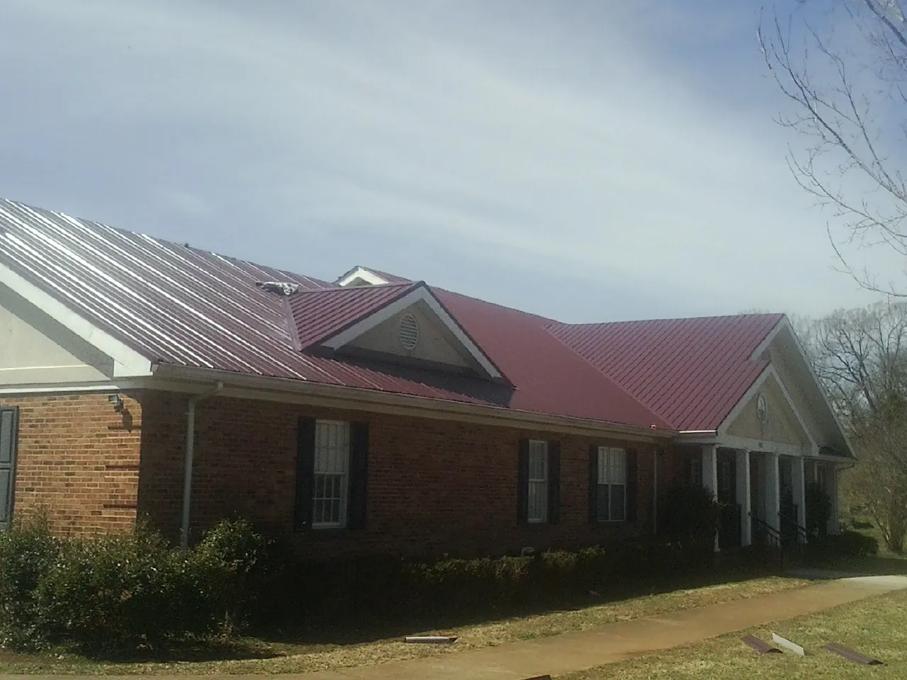 Red metal roof with gabled entries on a long brick building, from a Hail Damage Roof Repair job in Jenkintown