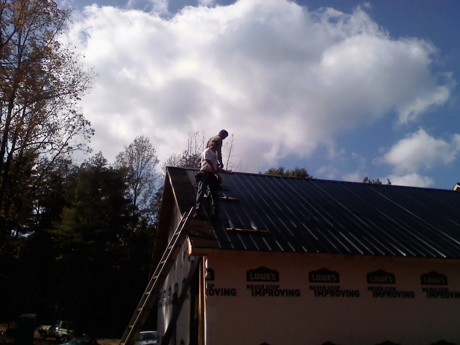 Roofer fastening dark metal panels high against a cloudy sky, from a Roof Inspection job in Jenkintown