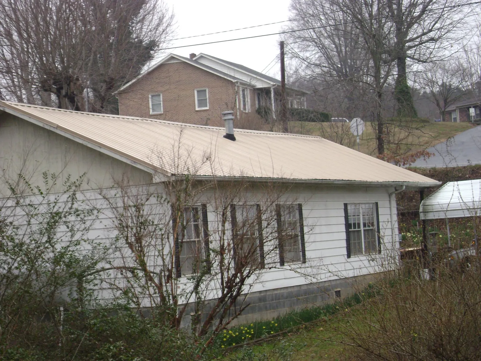 Tan metal roof on a white sided house set into a hillside — Commercial Roofing by Roofing Brothers in Jenkintown